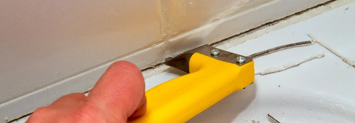 Hand entfernt Silikonfuge mit Werkzeug